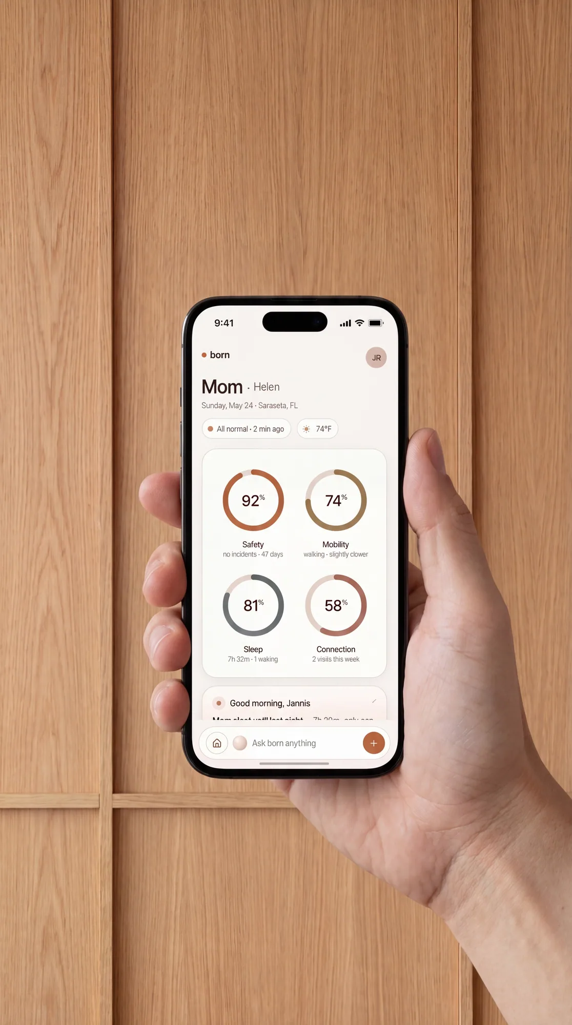 The Born app on a phone, held in a hand, showing the morning summary for Mom: 92% Safety, 74% Mobility, 81% Sleep, 58% Connection.